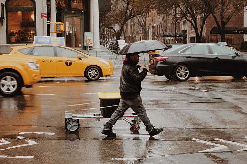 person man using umbrella walking along wet road automobile