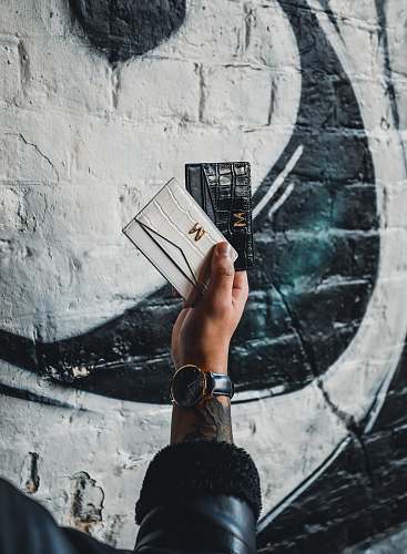 human person holding black and white leather wallets finger