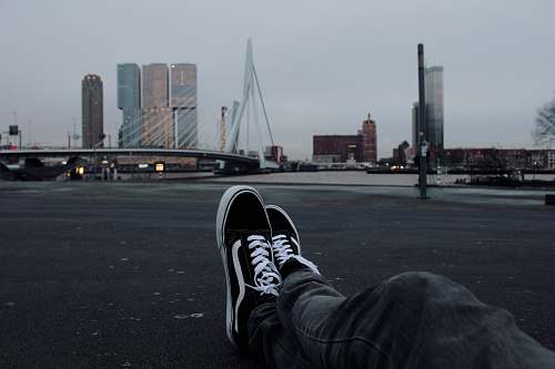 rotterdam person sitting on grey concrete road in front of white suspension bridge grey