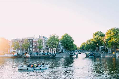 outdoors people riding canoe beside concrete bridge at daytime canal