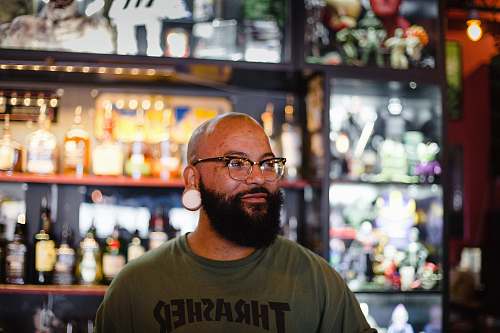 human man in gray Thrasher crew-neck shirt standing near rack of bottles people