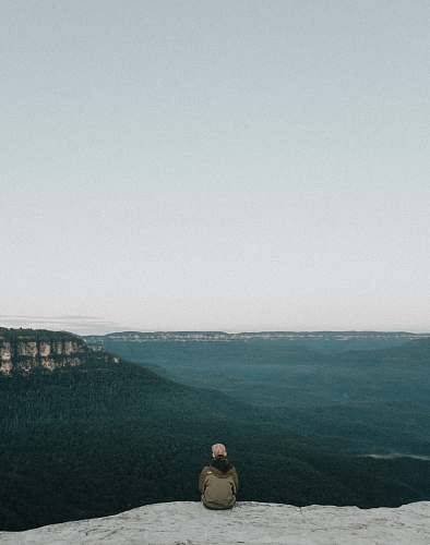 grey person sitting on rock while sight seeing blue mountains