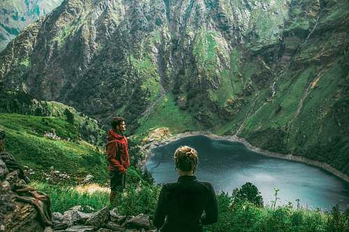 outdoors woman and man standing on mountain near creek during daytime mountain