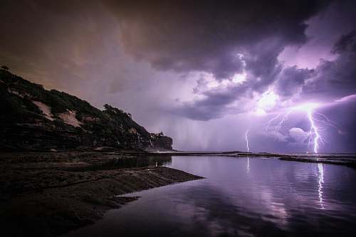 thunderstorm lightning near body of water and rock formation nature