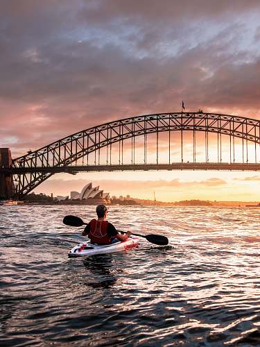 human person riding kayak towards metal bridge person