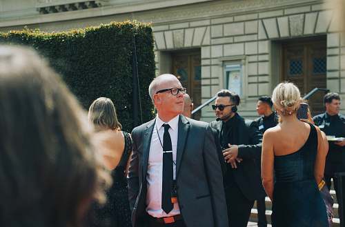 person man in black suit standing beside woman in black sleeveless dress accessory