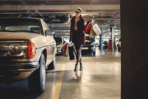 woman carrying shopping paper bags walking towards beige car inside parking lot