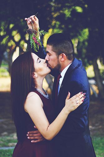 man and woman kissing near trees