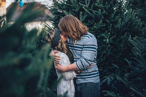 man kissing woman near pine tree
