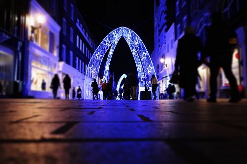 people walking near arched lighted decor between buildings
