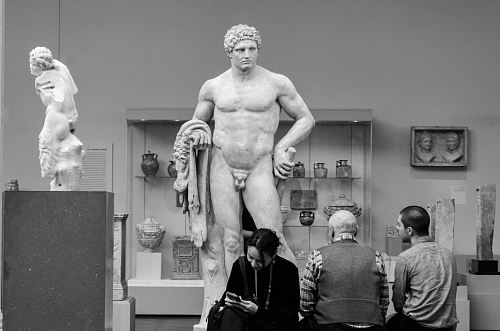 three people standing in front of naked man statue