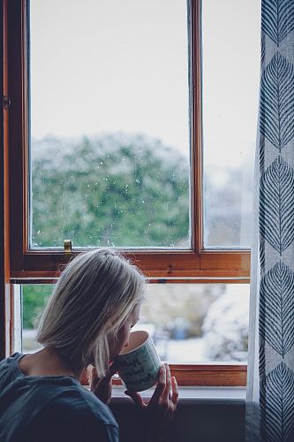 woman drinking in front of window at daytime