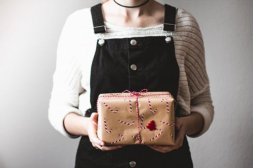woman holding brown gift box standing in front of white wall