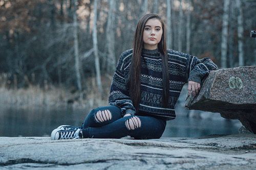 woman sitting on pavement hands against stone near body of water