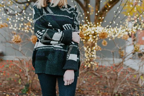 woman wearing sweater standing in front of plants and tree