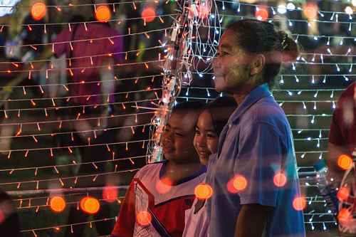 woman with girl and boy standing tunnel of string lights