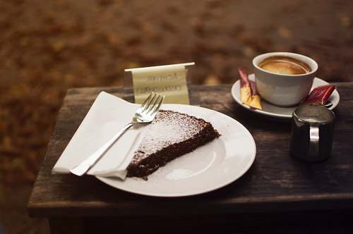 food plate of sliced cake with silver fork beside cup of coffe on brown wooden serving board dessert
