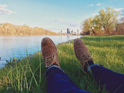 shoe person lying on grass front of body ofwater boot