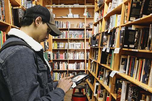 person man holding book beside bookshelf indoors