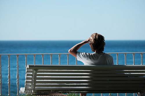people man sitting on bench near body of water during daytime person