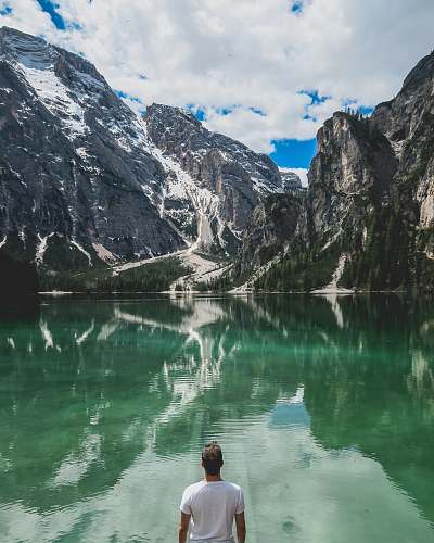 snow man standing in front of lake and cliff under white clouds and blue sky nature