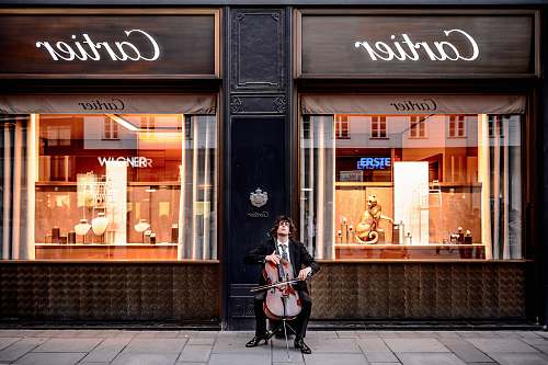 human man playing cello in front of store people