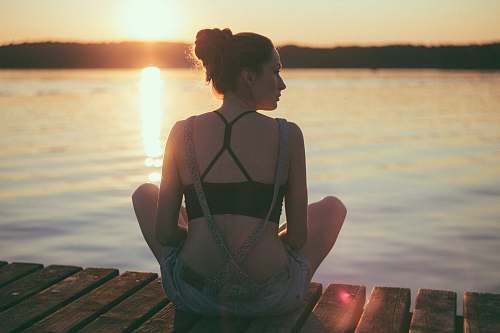 human woman sitting on brown wooden dock during sunset people