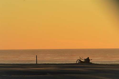 ocean person playing guitar in front of bicycle during daytime beach