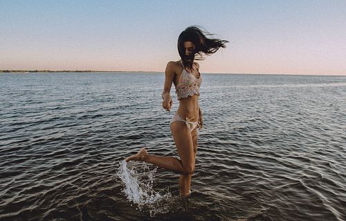 A girl in a bikini flicks her leg up behind her in the water at a beach