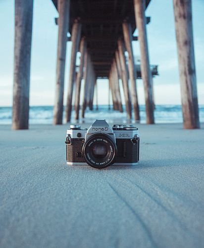 black and gray Canon AE-1 camera on gray sand under brown dock near body of water at daytime