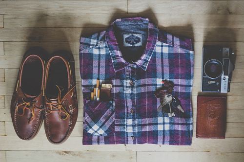 flat lay photography of button-up shirt, camera, keys, cigarettes, and pair of brown leather boat shoes