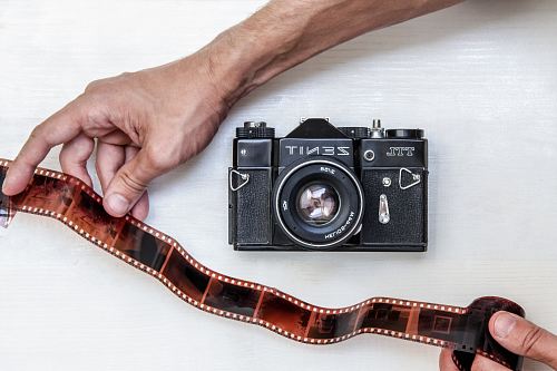 flat lay photography of person showing photo film beside Zenit DSLR camera