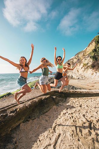four women jumping in sea shore during daytime