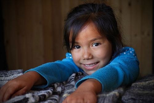 girl wearing blue sweater with hands on gray bedspread