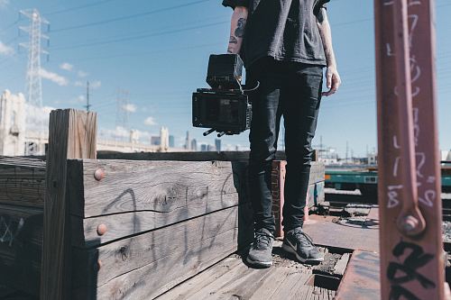 man holding black video camera while standing on plank