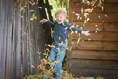 photo of boy near fence with falling leaves