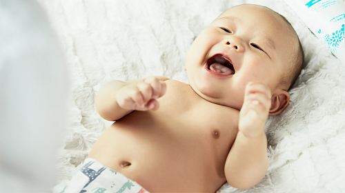 topless baby lying on bed smiling