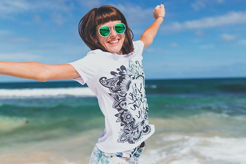 woman wearing white and black shirt jumping near seashore
