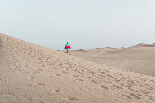 sand photo of person walking on desert holding red box soil