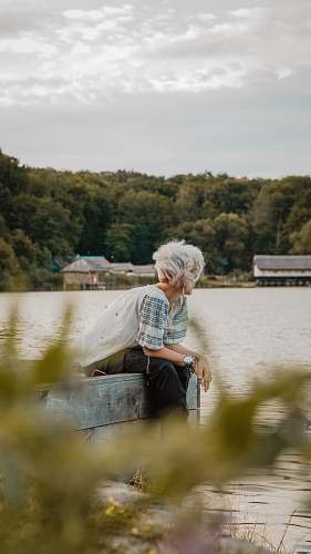 apparel man sitting on wooden dock during daytime clothing