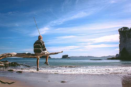 outdoors person sitting on driftwood near seashore during daytime water