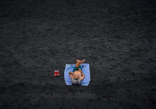person shirtless man lying on blue picnic mat on the field sand