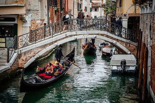human people riding boat near bridge with people crossing during daytime gondola