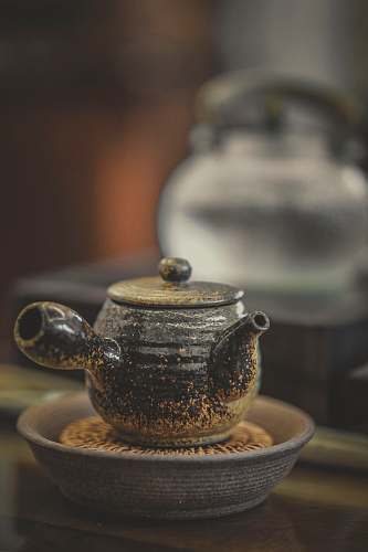 saucer close-up photography of black ceramic pot on brown surface teapot