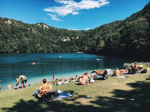 lake group of people gathering near lake under blue sky during daytime tree