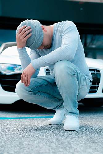 human man wearing grey long-sleeved shirt sitting on ground while holding his knit cap people