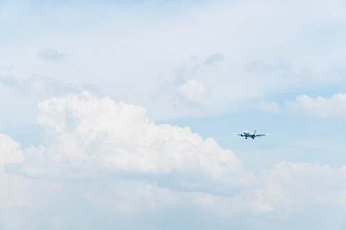 blue photo of white commercial airplane flying in sky under white clouds flying
