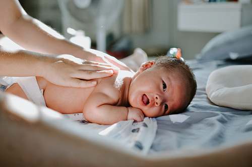 human baby laying on bed while woman massaging his back person