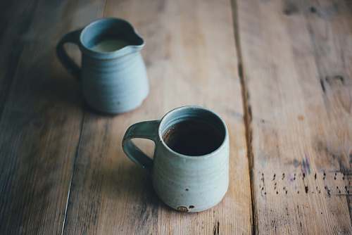 cup white ceramic mug with brown and white liquid inside on brown wooden surface table