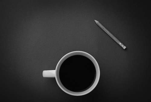 black-and-white white ceramic teacup near gray pencil on black surface black